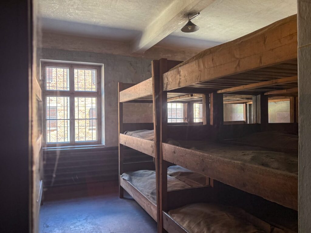 Blick in Unterkunftsraum in Auschwitz I mit einfachen Holzpritschen und spärlicher Einrichtung