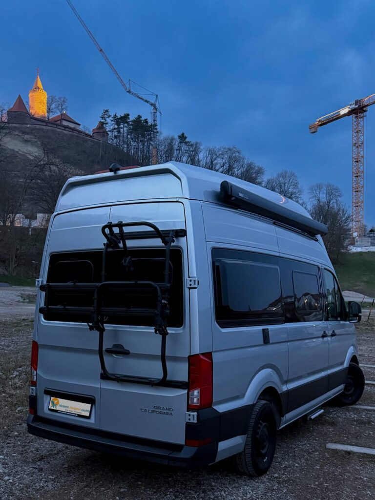 Campervan auf dem Parkplatz im Abendlicht unterhalb der angeleuchteten Leuchtenburg.