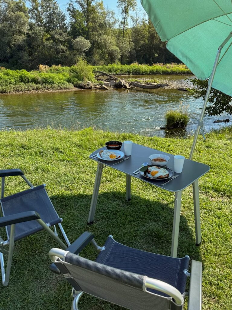Mittagessen am Fluss Strei mit Campingtisch, zwei Stühlen und grünem Sonnenschirm in Rumänien