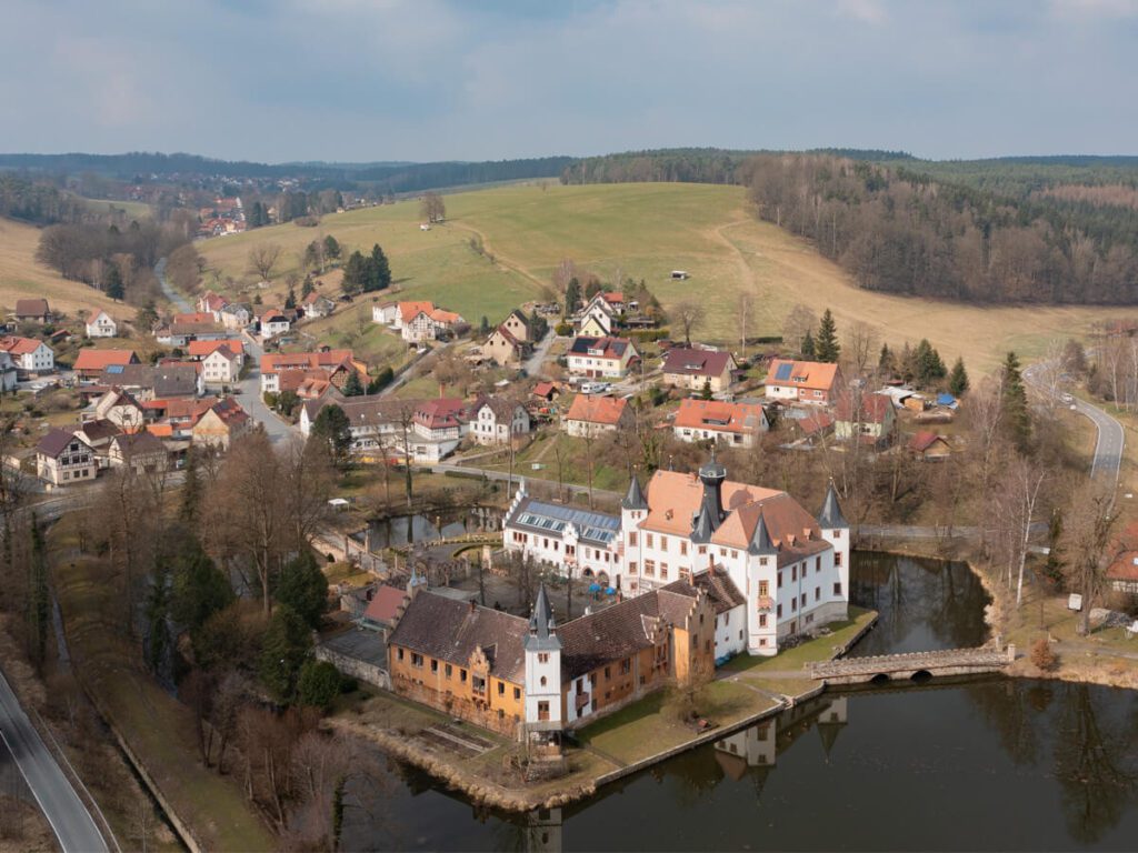 Luftbild vom Schloss Fröhliche Wiederkunft in Trockenborn-Wolfersdorf mit Teich, Feldern und Dorf.