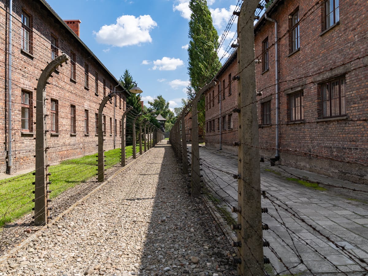 Blick entlang des Stacheldrahtzauns zwischen Backsteingebäuden in Auschwitz-Birkenau