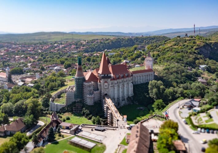 Luftaufnahme der Burg Corvin in Hunedoara, Rumänien, mit Stadt und grünen Hügeln im Hintergrund