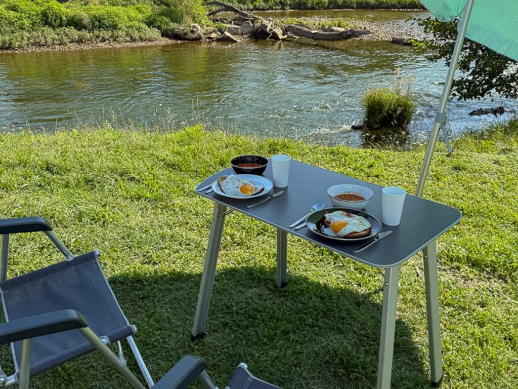 Frühstück mit Spiegeleiern und Bohnen am Flussufer beim Camping