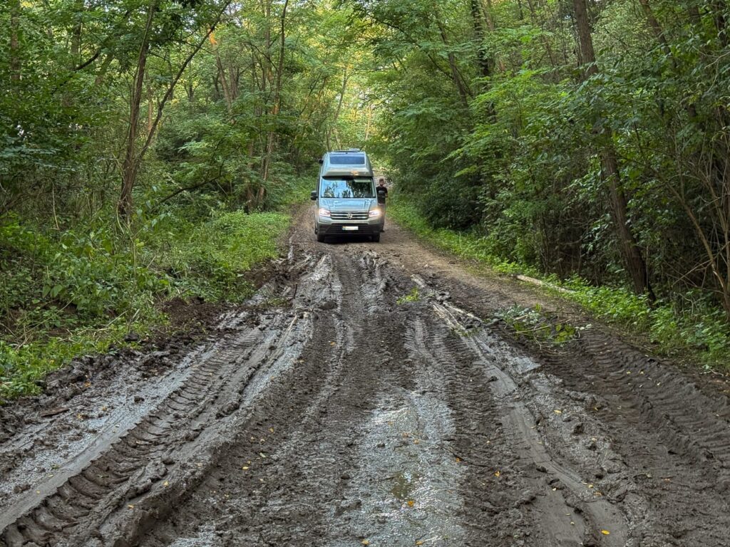 VW Grand California im Schlamm auf einem Waldweg in Rumänien, mitten im Offroad-Abenteuer.