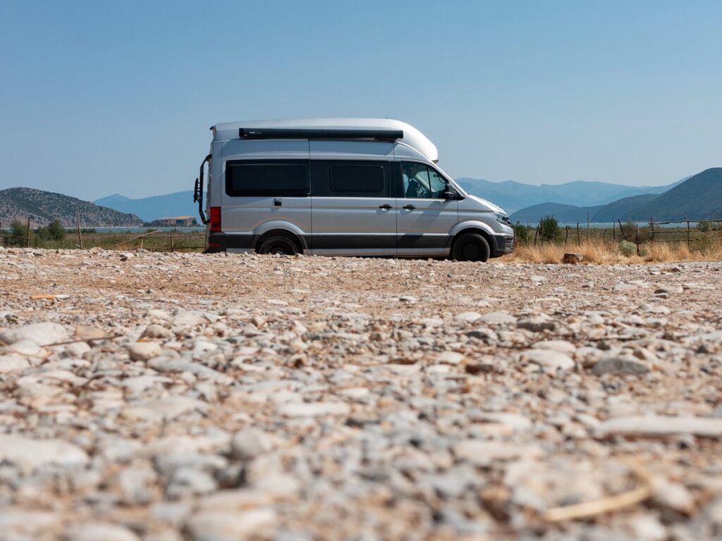Camper auf Schotterpiste mit Bergen und See im Hintergrund