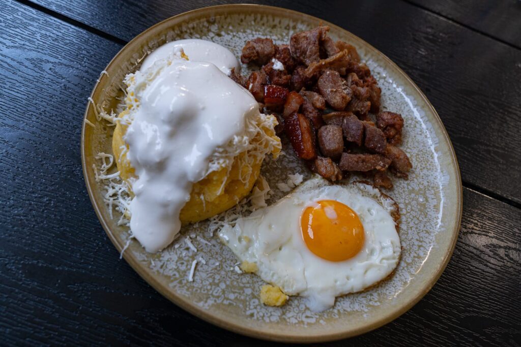 Rumänisches Gericht Tochitură de porc mit Polenta, Käse, Schmand und Spiegelei