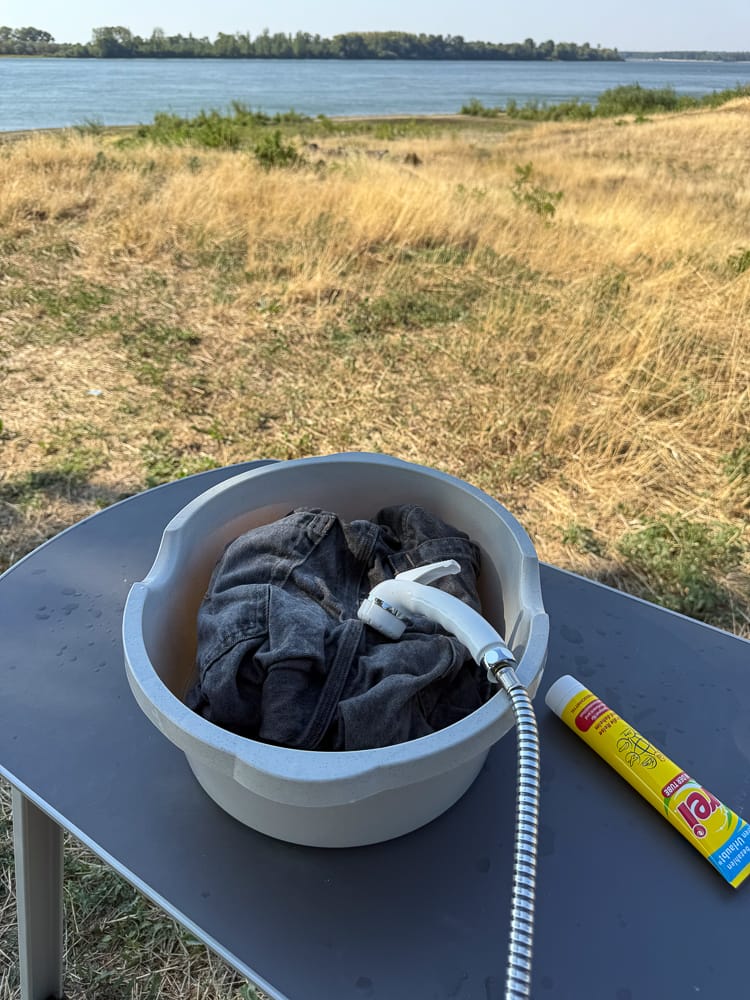 Camping-Alltag: Wäsche waschen mit Schüssel und Camperdusche direkt am Ufer der Donau.