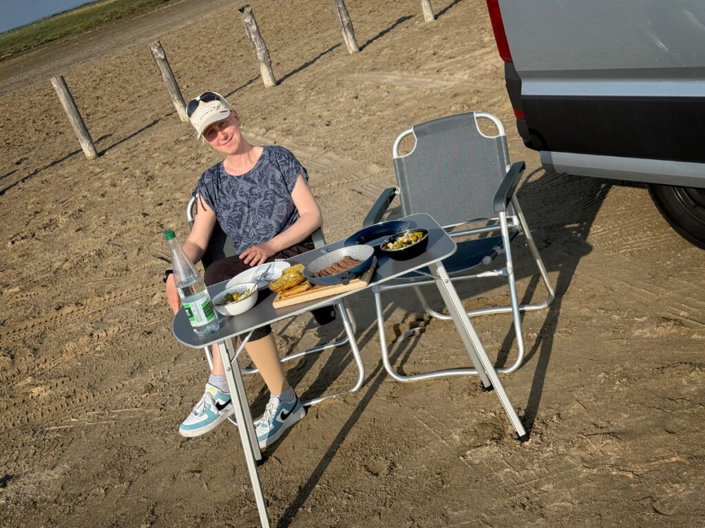 Dani sitzt beim Abendessen am Strand von Salin-de-Giraud neben dem Camper in der Abendsonne