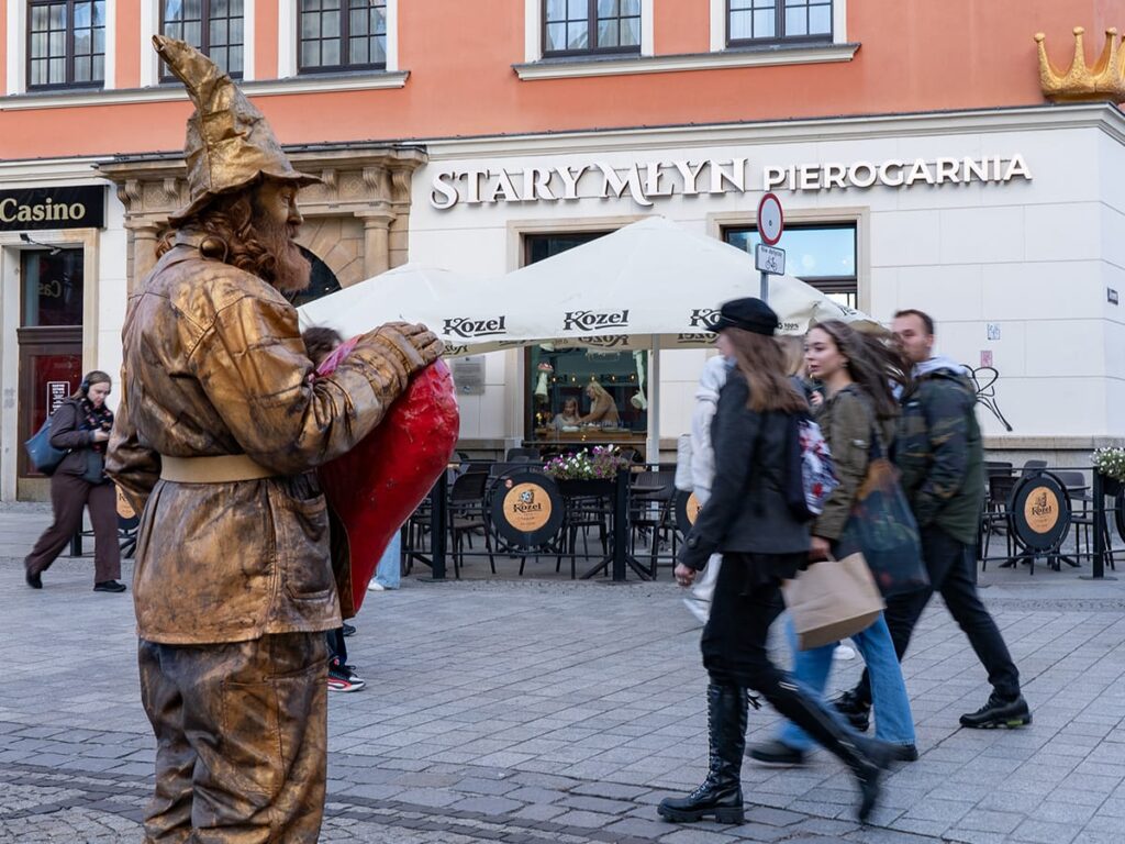 Straßenszene vor dem Restaurant Pierogarnia Stary Młyn in Breslau mit einer lebenden Statue und Passanten