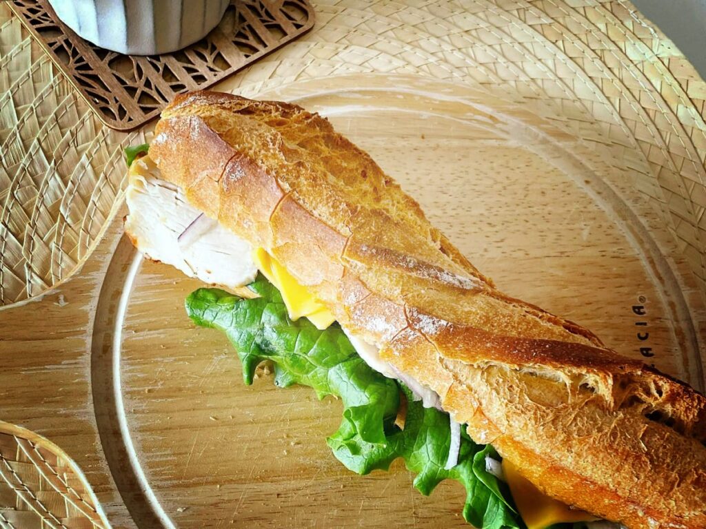 Frisches Baguette mit Salat, Käse und Hähnchen und Kaffee in einem Bistro.