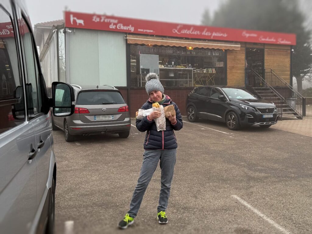 Dani steht im Winter vor der Bäckerei La Ferme de Charly in Lyon und zählt die Tüte mit frischen Baguettes