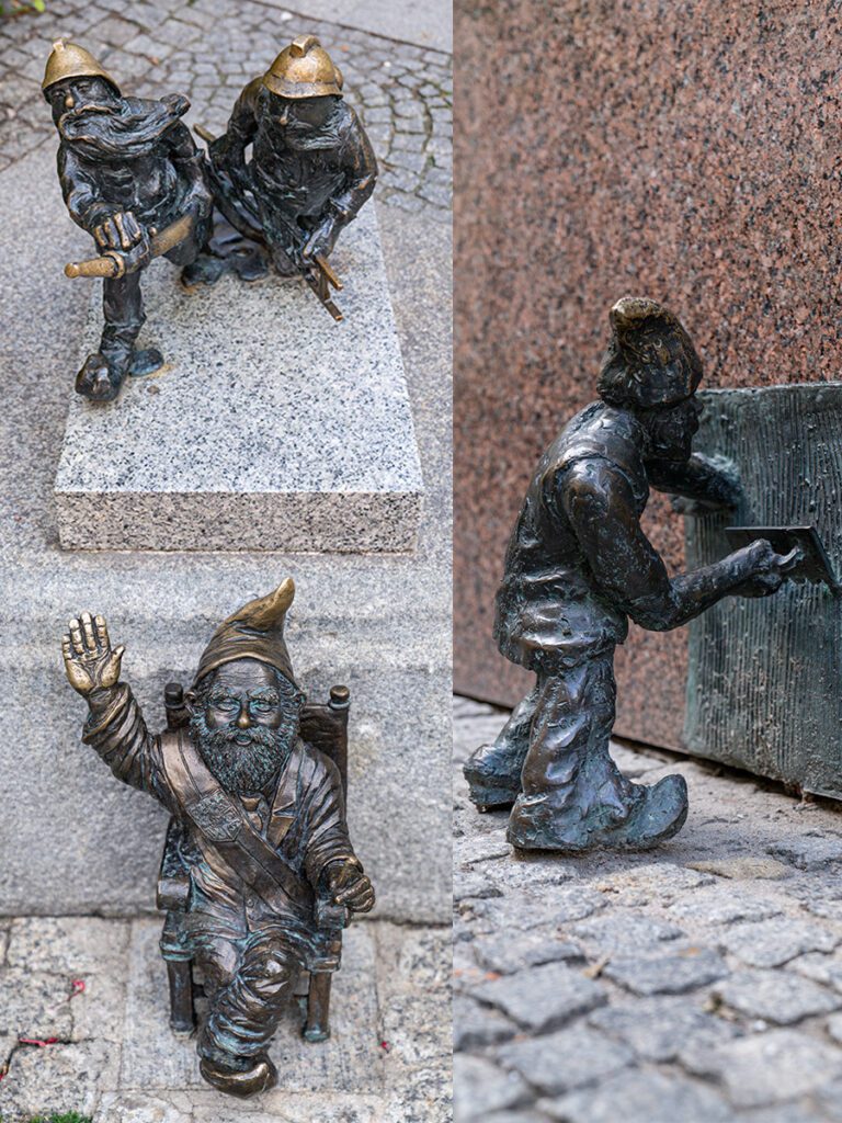 Zwei Breslauer Zwerge als Feuerwehrleute mit Helm und Schlauch sowie ein weiterer Zwerg auf einem Stuhl in der Altstadt