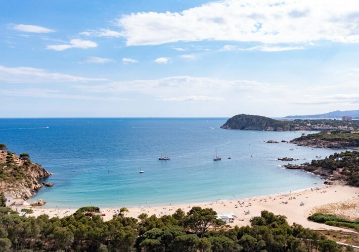 Drohne blick auf eine türkisfarbene Bucht mit Sandstrand und Segelbooten bei Roses an der Costa Brava.
