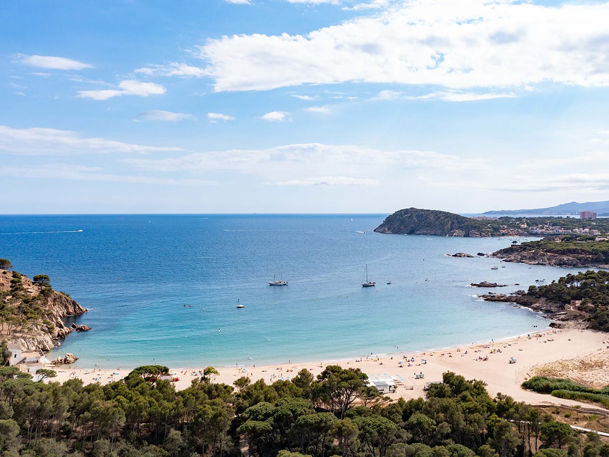 Drohne blick auf eine türkisfarbene Bucht mit Sandstrand und Segelbooten bei Roses an der Costa Brava.