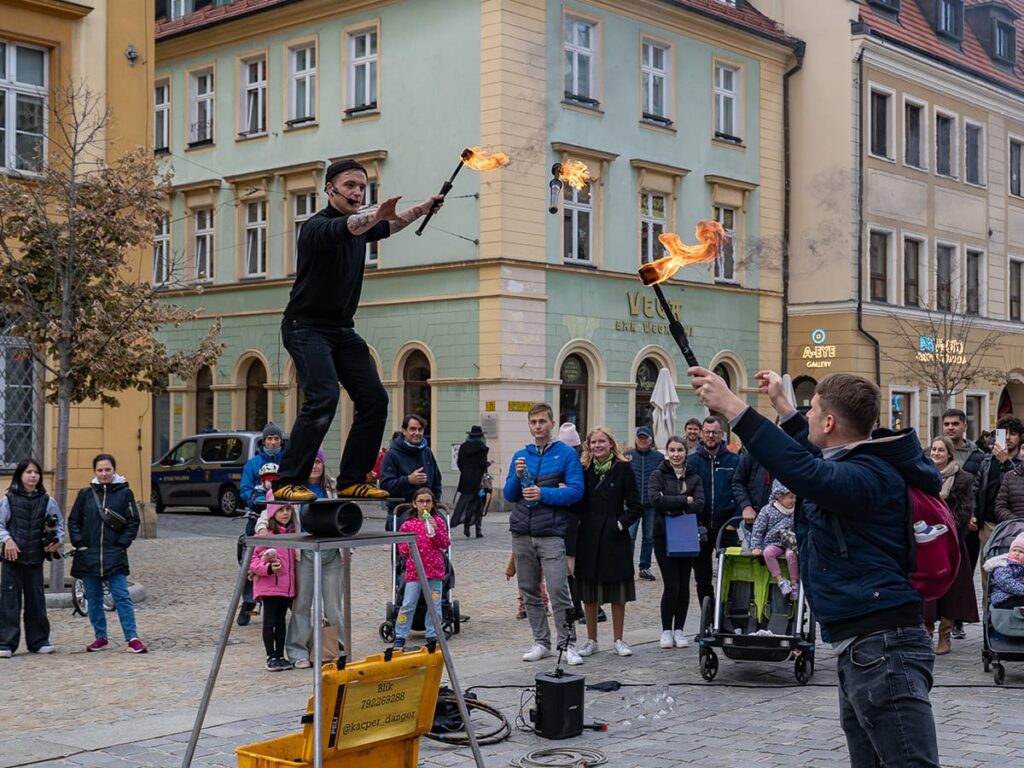 Straßenkünstler jongliert mit brennenden Fackeln auf dem Marktplatz in Breslau, umgeben von Zuschauern