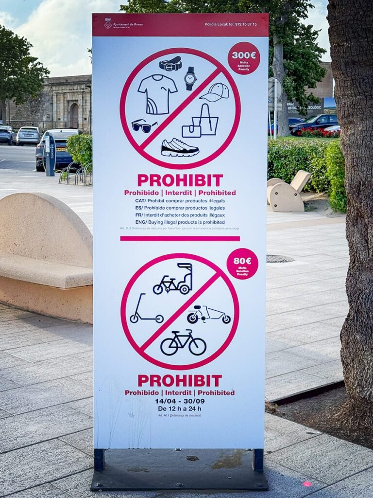 Verbotsschild an der Promenade von Roses mit Piktogrammen für E-Scooter, Fahrräder und Straßenverkäufe.