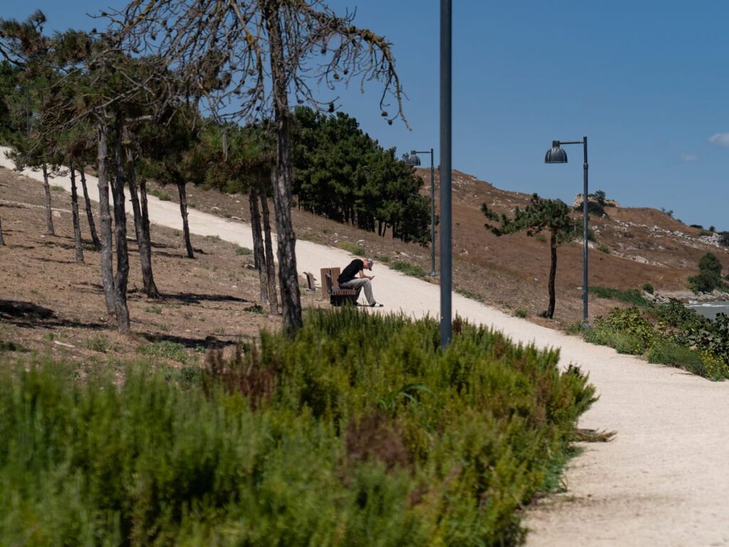 Mein Sohn sitzt auf einer Parkbank im Büyüçekmece-Park mit Blick auf den See und die umliegenden Hügel