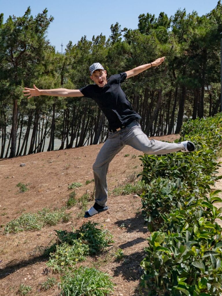 Pius springt im Büyüçekmece-Park über eine niedrige Hecke mit dem See und Kiefernwald im Hintergrund