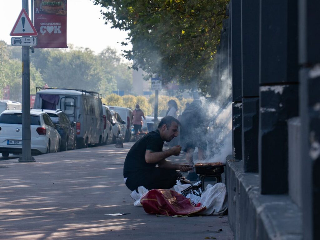 Mann grillt Hähnchen auf einem kleinen Holzkohlegrill am Bürgersteig vor dem Hasbahçe-Park in Istanbul