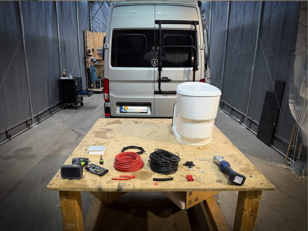 Clesana Toilette und Einbauzubehör auf Werkstatttisch vor VW Grand California