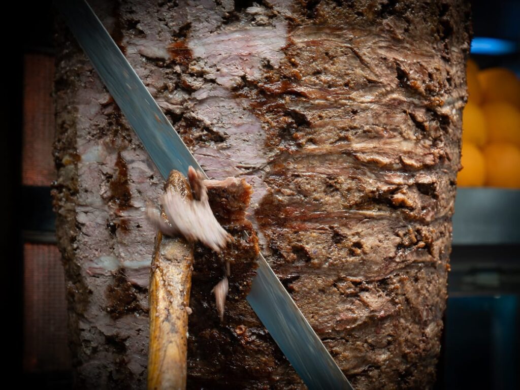 Naheaufnahme eines Döner-Spießes in Istanbul, bei dem frisch geschnittenes Fleisch mit einem langen Messer abgetragen wird