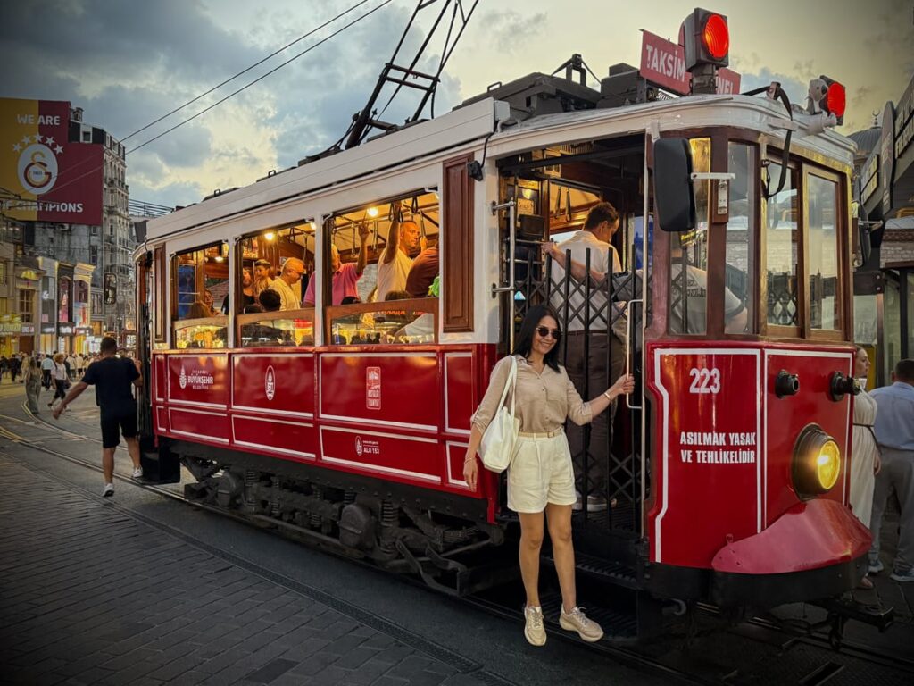 Nostalgische rote Straßenbahn der Istiklal Caddesi in Istanbul, voller Menschen im Abendlicht vor dem Taksim-Platz.