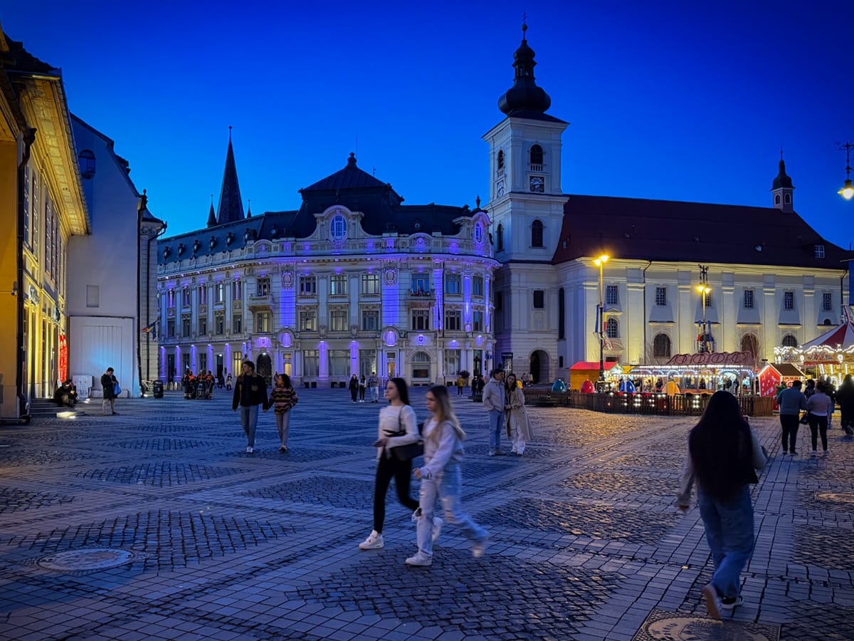 Abendstimmung auf dem Großen Ring in Sibiu mit beleuchteten Gebäuden und Menschen auf dem Platz