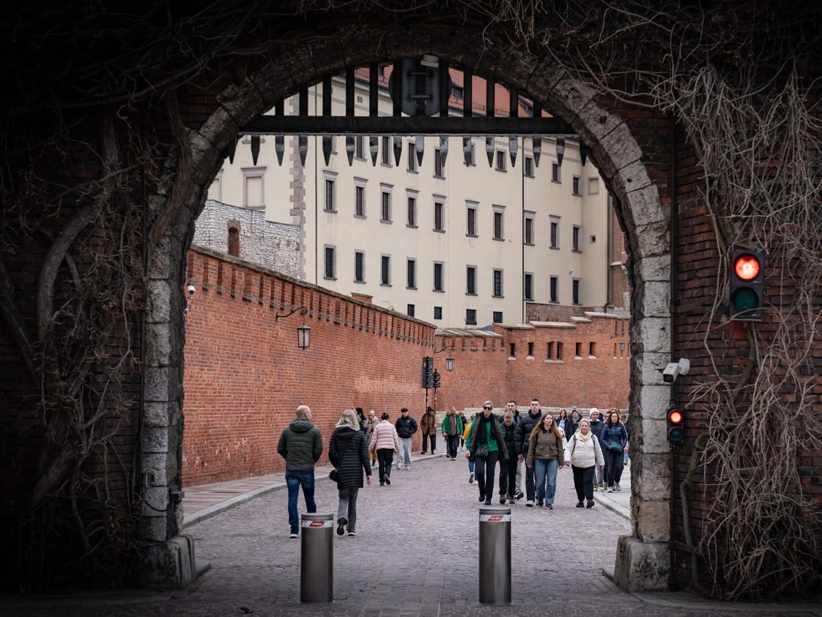 Menschen gehen durch ein historisches Tor am Wawel in Krakau entlang der roten Backsteinmauer