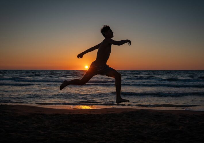 Silhouette eines springenden Jugendlichen bei Sonnenuntergang am Meer in Albanien