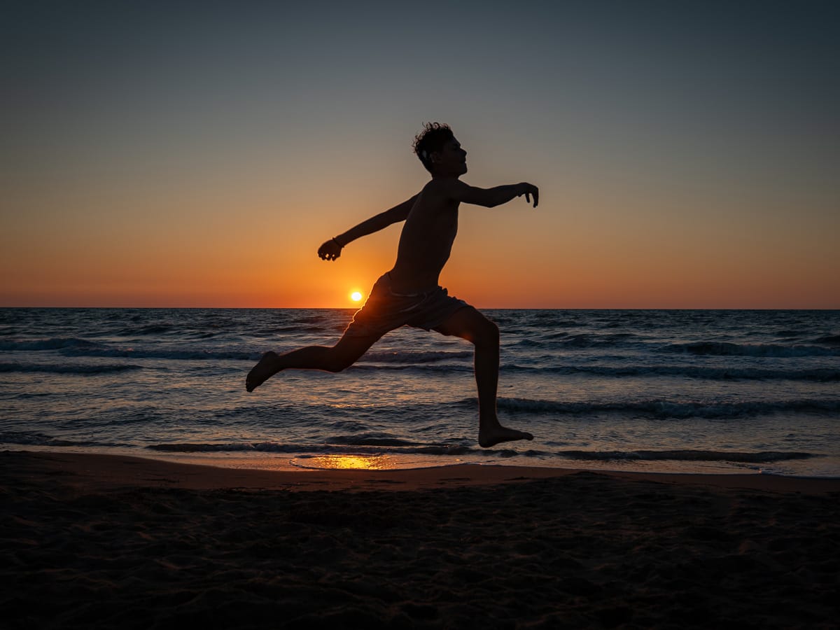 Silhouette eines springenden Jugendlichen bei Sonnenuntergang am Meer in Albanien