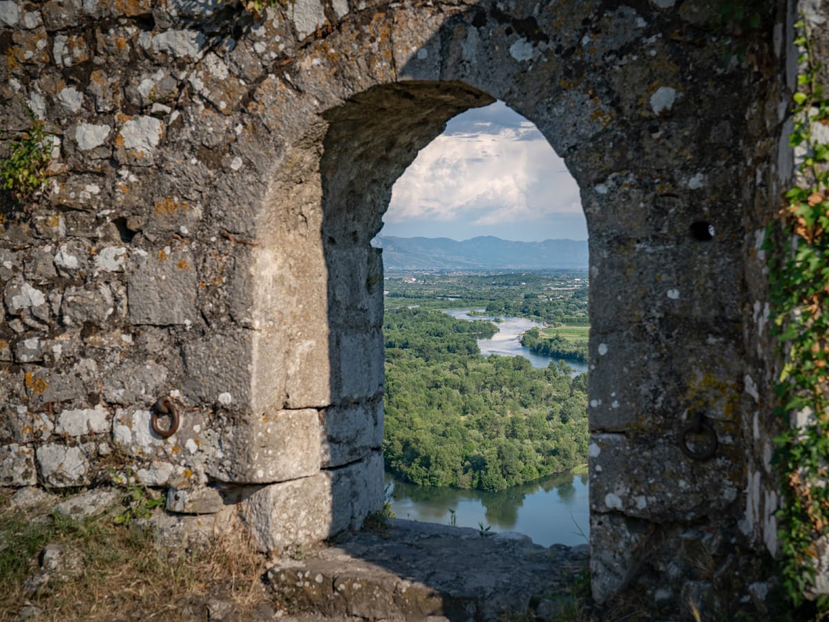 Blick durch einen Mauerbogen der Burg Rozafa auf die Flusslandschaft unterhalb der Festung.