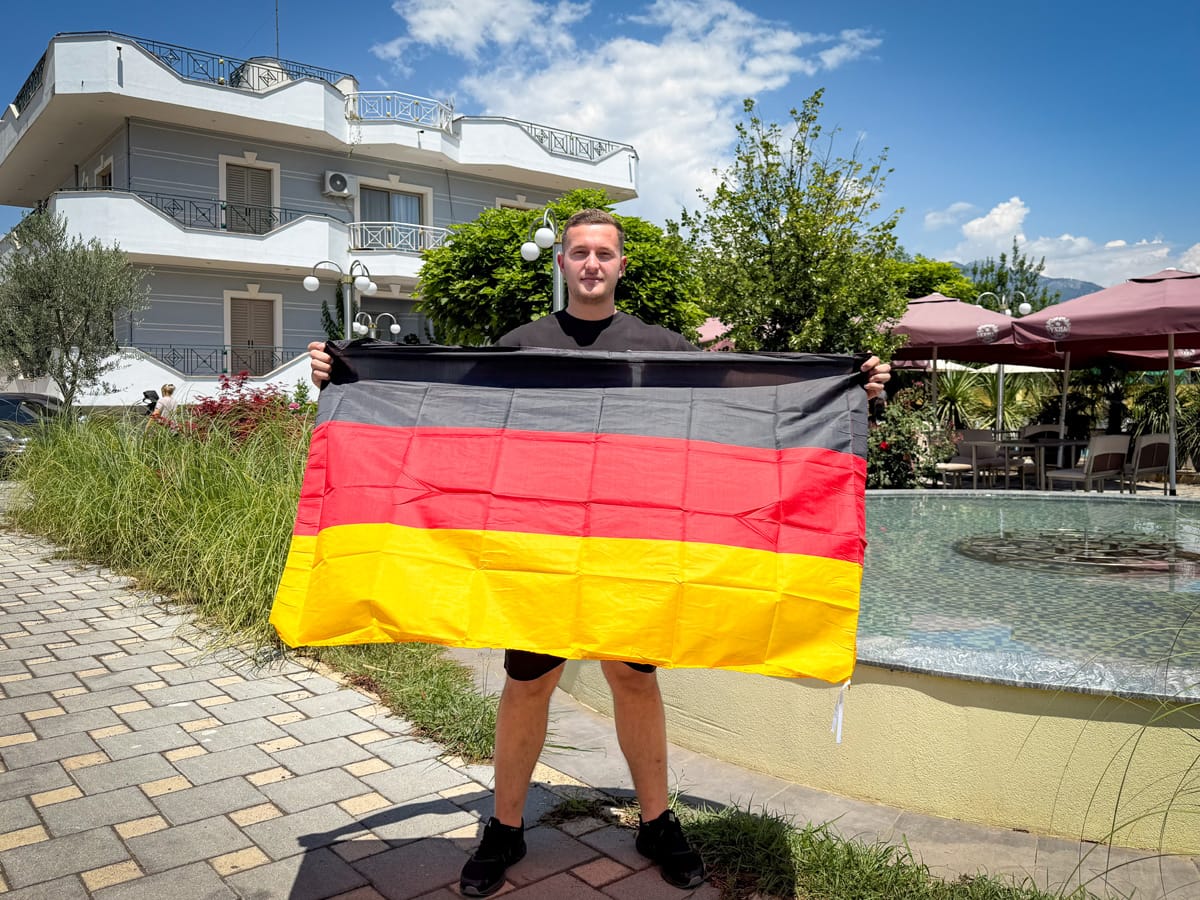 Sohn des Hotelbesitzers mit der Deutschland-Flagge vor dem Bar Restaurant Union in Postribë