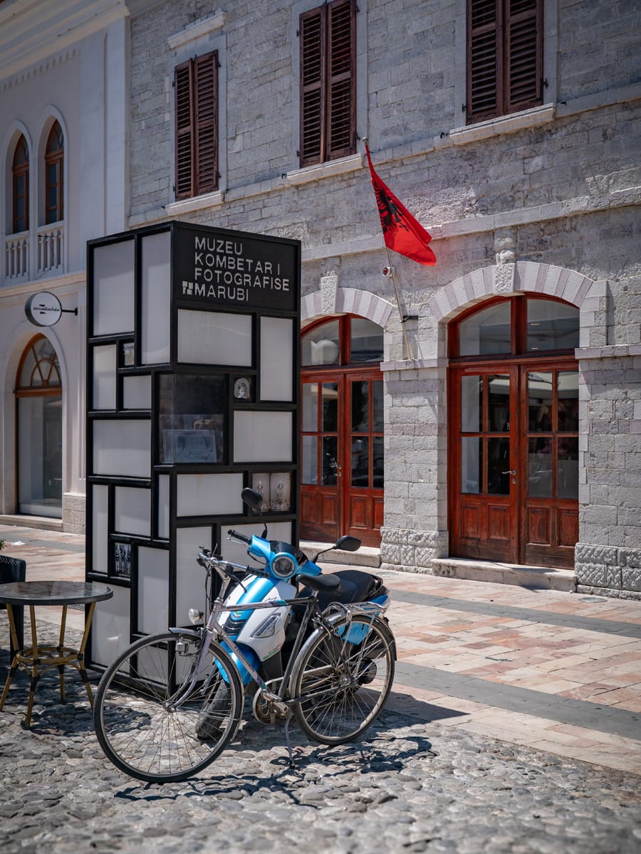 Außenansicht des Marubi-Museums in Shkodra mit Litfaßsäule und albanischer Flagge