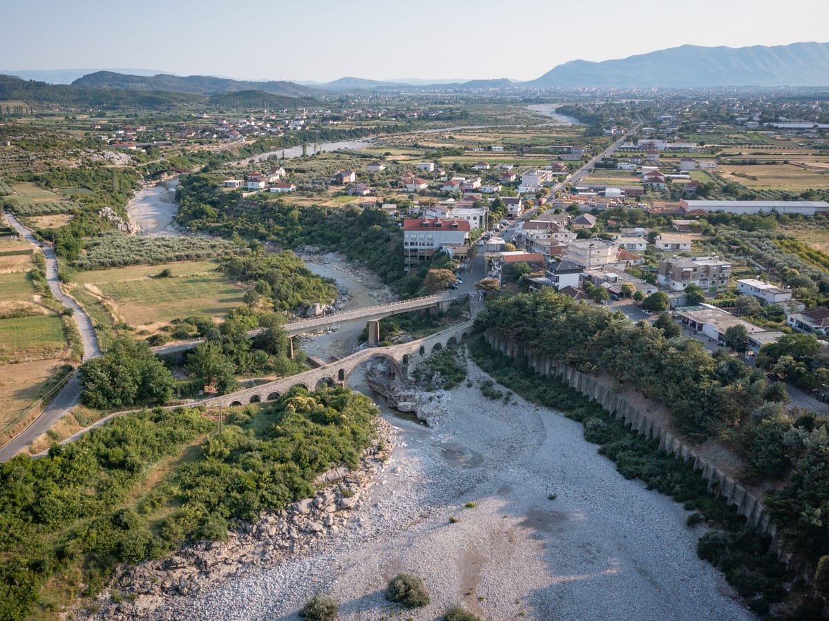 Drohnenaufnahme der Mes-Brücke (Ura e Mesit) bei Shkodra mit moderner Straßenbrücke und dem Kir-Fluss