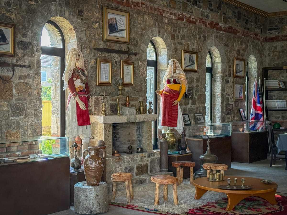 Historischer Wohnraum mit Kamin, Trachtenpuppen, Kupfergefäßen und traditionellen Möbeln im Ethnografischen Museum von Postribë.
