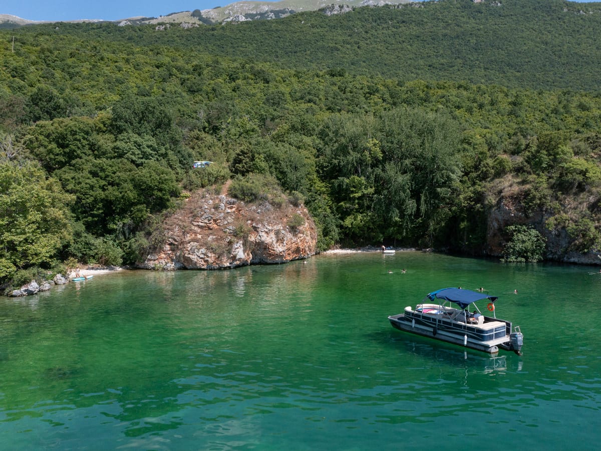 Ausflugsboot in einer kleinen Badebucht am Südufer des Ohridsees mit kristallklarem, türkisgrünem Wasser.
