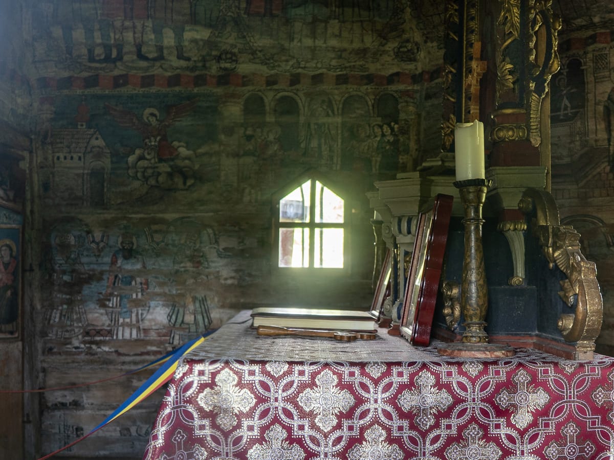 Innenraum der UNESCO-Holzkirche in Bârsana mit Altar, historischen Wandmalereien und einem kleinen Fenster.