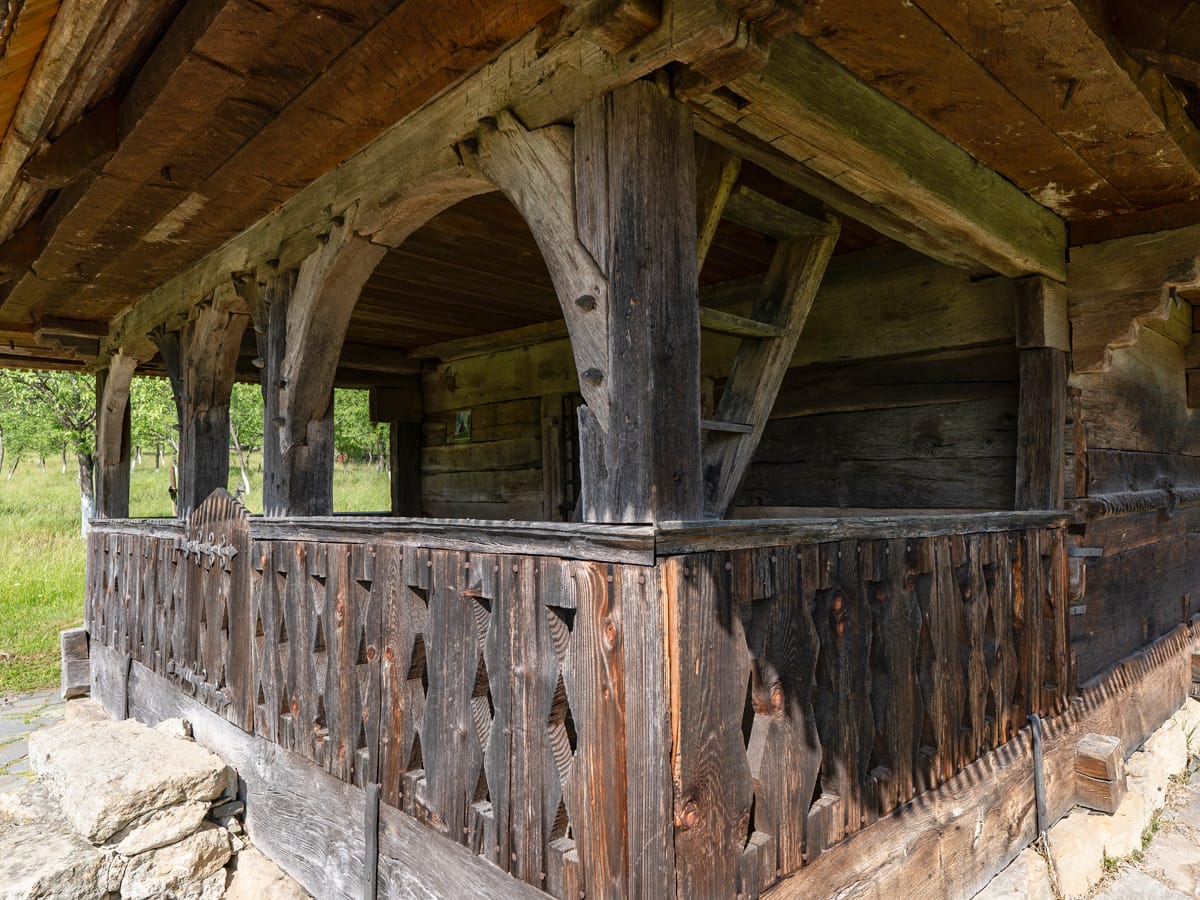 Überdachte Vorhalle der UNESCO-Holzkirche in Bârsana mit geschnitzten Eichensäulen und hölzerner Brüstung.