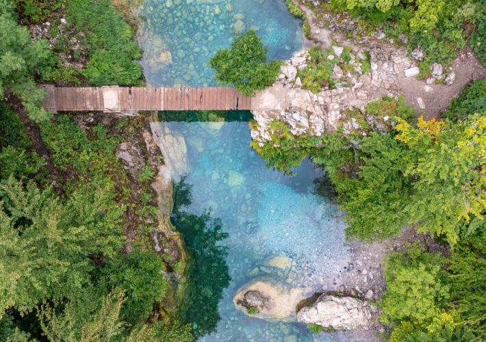 Holzbrücke über den türkisfarbenen Fluss am Blue Eye bei Theth in den Albanischen Alpen aus der Drohnenperspektive