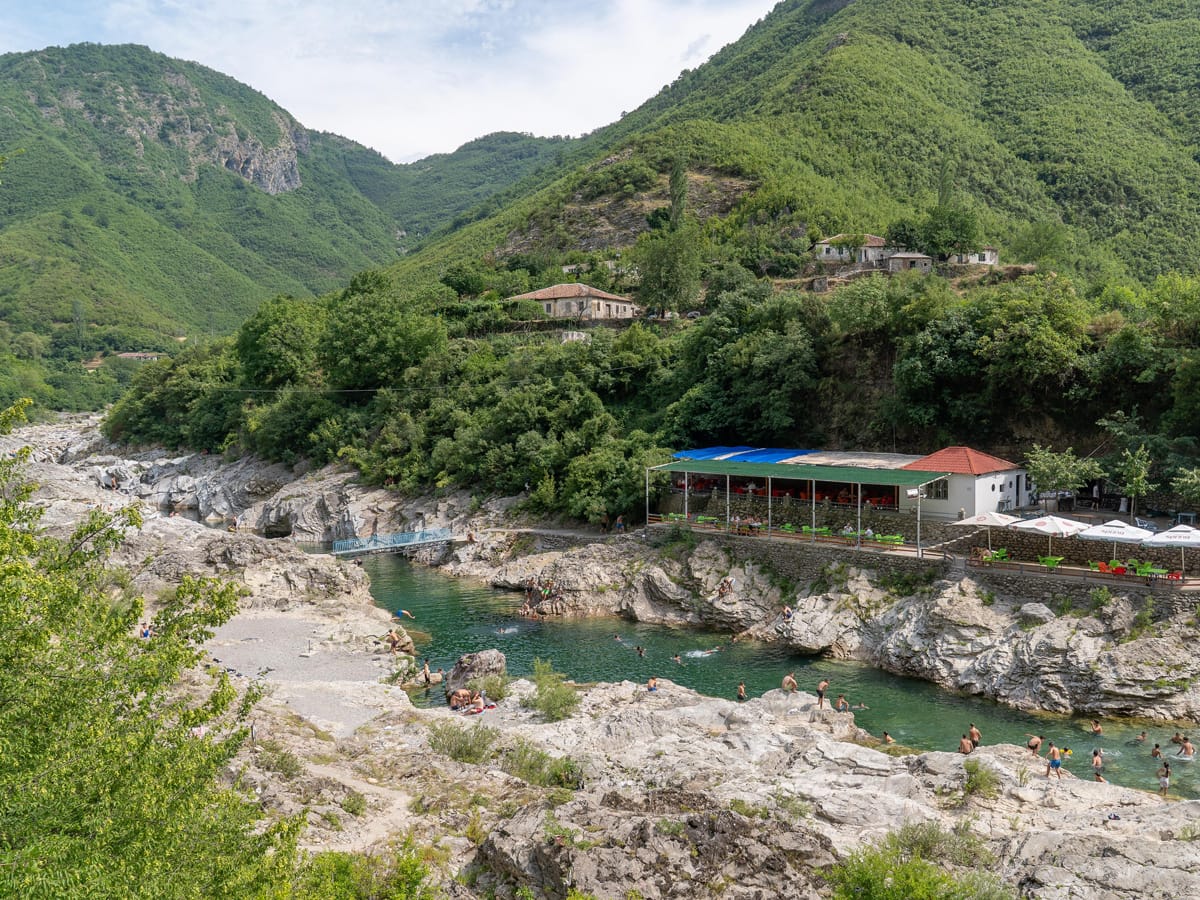 Badestelle am Kir-Fluss bei Prekal mit kristallklarem, smaragdgrünem Wasser, Kalksteinfelsen und Restaurant im Hintergrund.