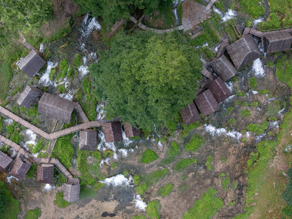 Drohnenaufnahme der historischen Pliva-Wassermühlen bei Jajce mit Holzstegen und zahlreichen Wasserläufen.