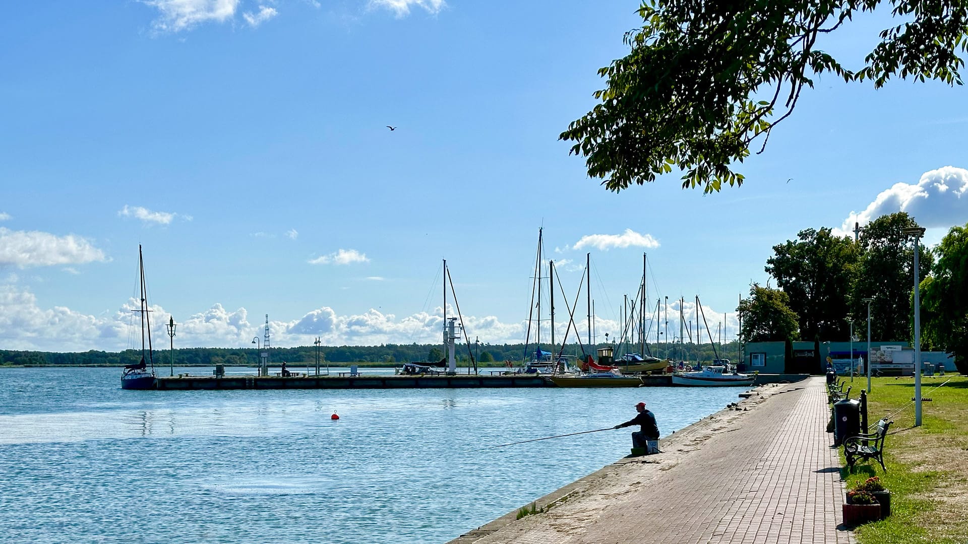 Ruhiger Hafen von Nowe Warpno in Polen mit Segelbooten, Promenade und Angler am Wasser