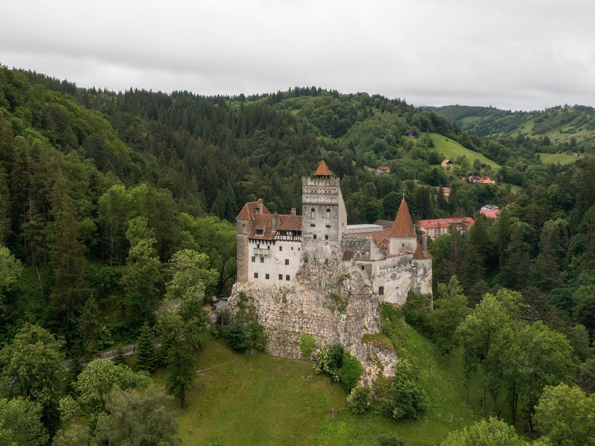 Drohnenaufnahme von Schloss Bran auf seinem Felsen inmitten der bewaldeten Hügellandschaft Siebenbürgens.