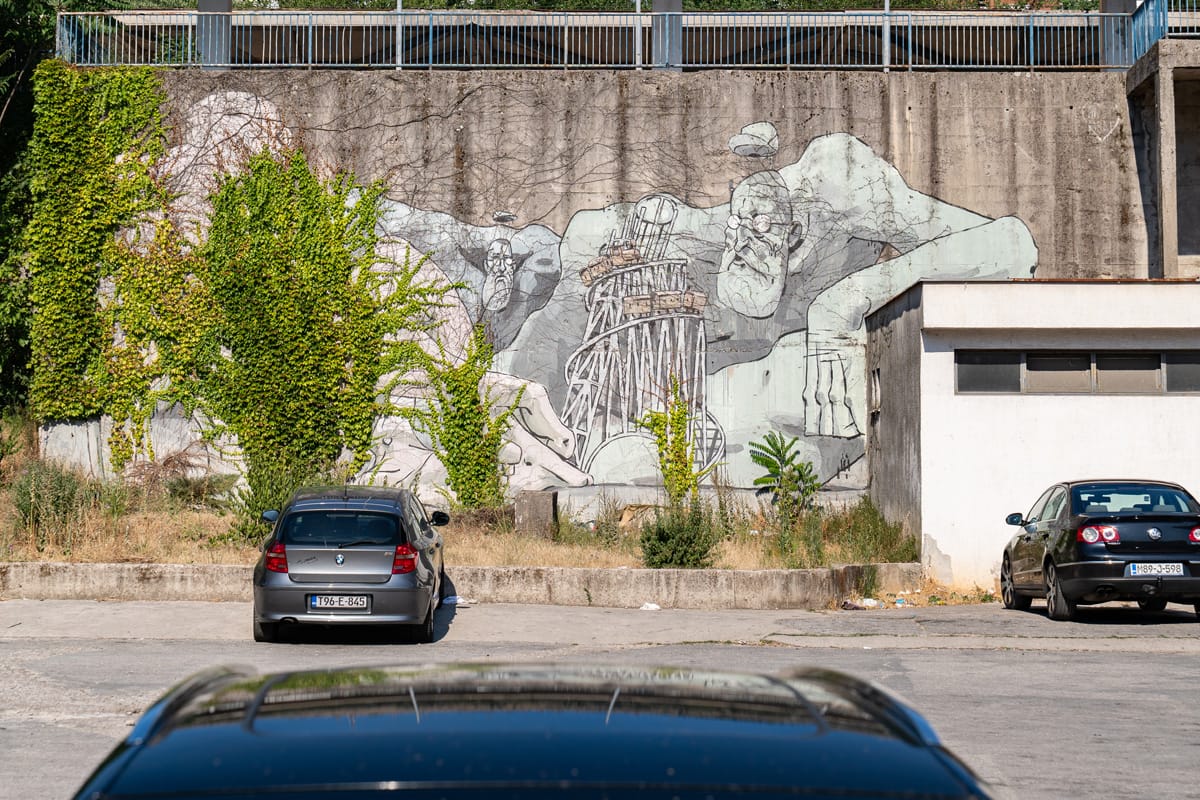 Großes Street-Art-Mural auf einer Betonwand in Mostar, teilweise von Efeu überwachsen