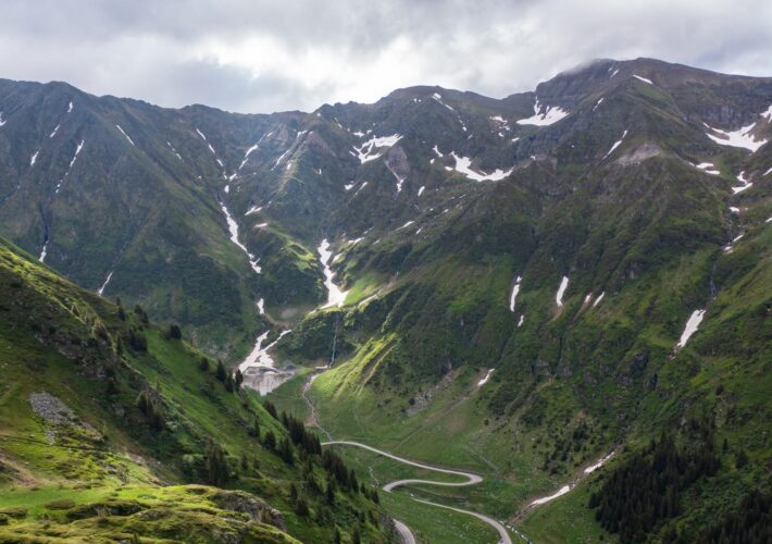 Panoramablick auf die Transfăgărășan mit Serpentinen und schneebedeckten Gipfeln der Karpaten in Rumänien.