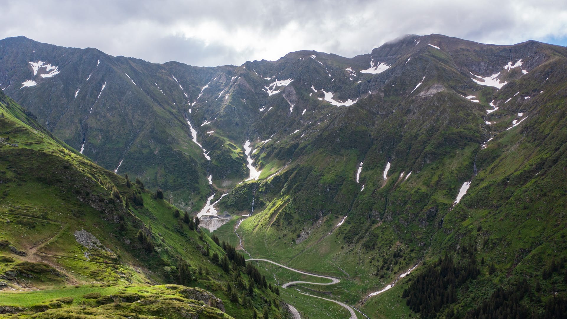Panoramablick auf die Transfăgărășan mit Serpentinen und schneebedeckten Gipfeln der Karpaten in Rumänien.