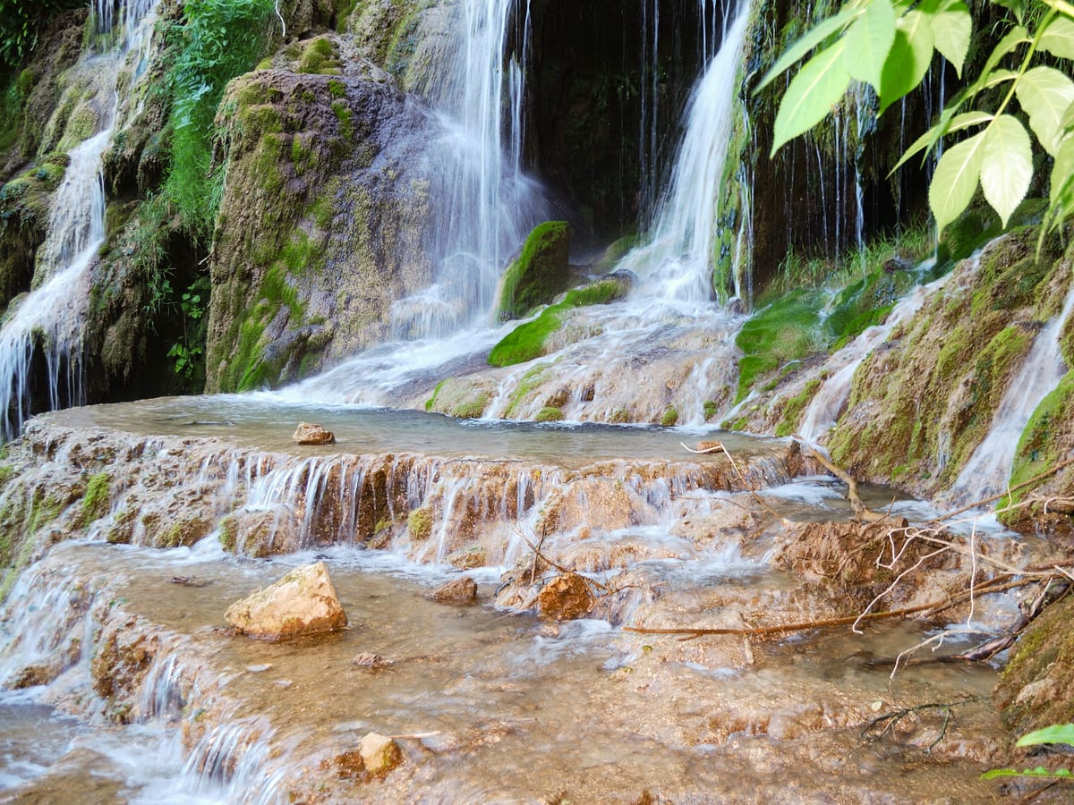 Wasser fließt über flache Kalksinterstufen und moosbewachsene Felsen an den Krushuna-Wasserfällen in Bulgarien.