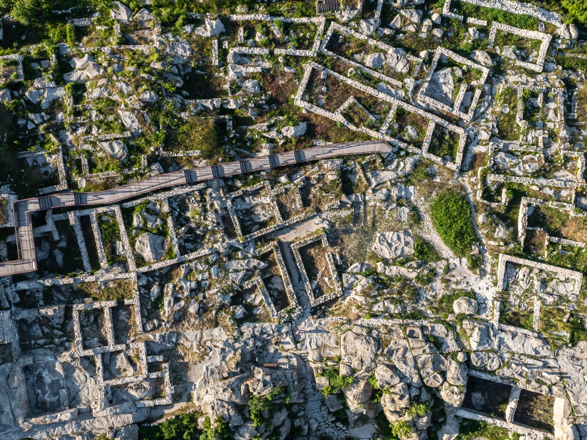Senkrechte Luftaufnahme von Perperikon mit steinernen Raumgrundrissen, bearbeiteten Felsen und hölzernen Besucherstegen.