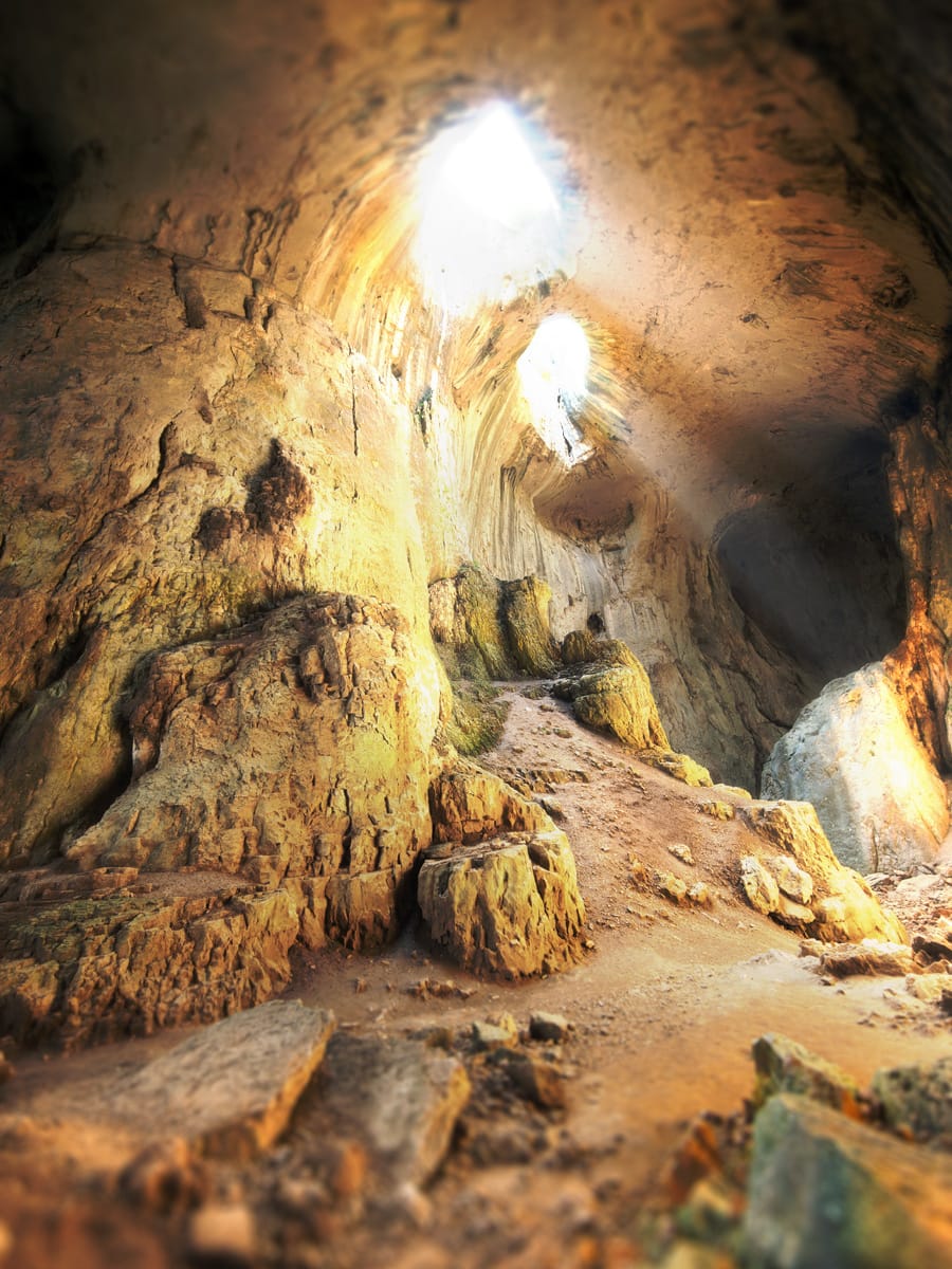Blick in die Prohodna-Höhle mit zwei hellen Deckenöffnungen, den „Augen Gottes“, über zerklüfteten Felsen.