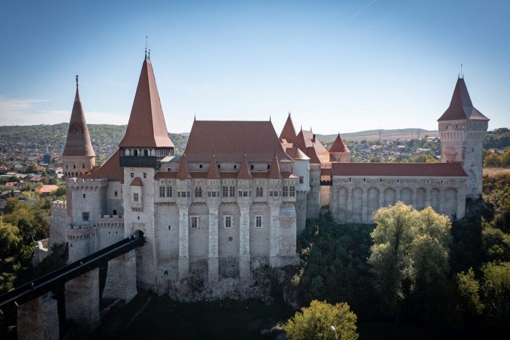 Luftaufnahme der Burg Corvin in Hunedoara, Rumänien, mit ihren markanten Türmen, roten Ziegeldächern, mächtigen Festungsmauern und der langen Zugangsbrücke.